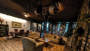 A cozy living room with patterned furniture, a tiled floor, and a large window offering a view of the outdoors. - The Art History House, indoor heated pool, 3 bedrooms, with two kitchens (Goose Creek)