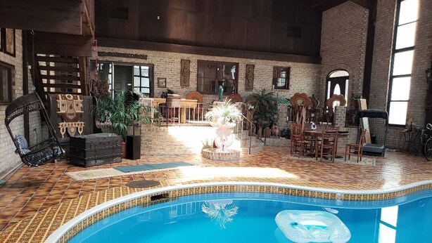 An indoor swimming pool with a tiled floor, surrounded by wooden furniture and potted plants. - The Art History House, indoor heated pool, 3 bedrooms, with two kitchens (Goose Creek)