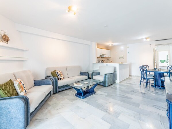 A modern living room with a sofa, armchairs, a coffee table, and a dining area with chairs and a table.