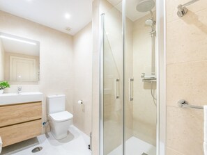 A modern bathroom with a glass-enclosed shower, a white toilet, and a wooden vanity with a mirror.