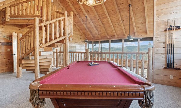 A pool table in a wooden cabin with a view of mountains.