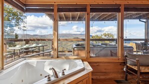A wooden cabin with a large bathtub, a dining area with a table and chairs, and a hot tub. - Serenity - Mountain VIEWS From Every Room! - 71 Windows (Sevierville)