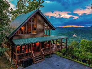 A log cabin with a large porch and a scenic mountain view.