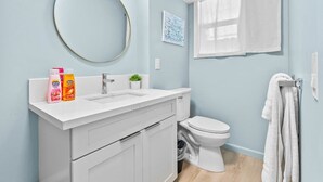 A bathroom with a white sink, a toilet, a round mirror, and a towel rack.