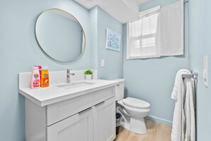 Un baño con un lavabo blanco, un inodoro, un espejo redondo y un perchero para toallas.