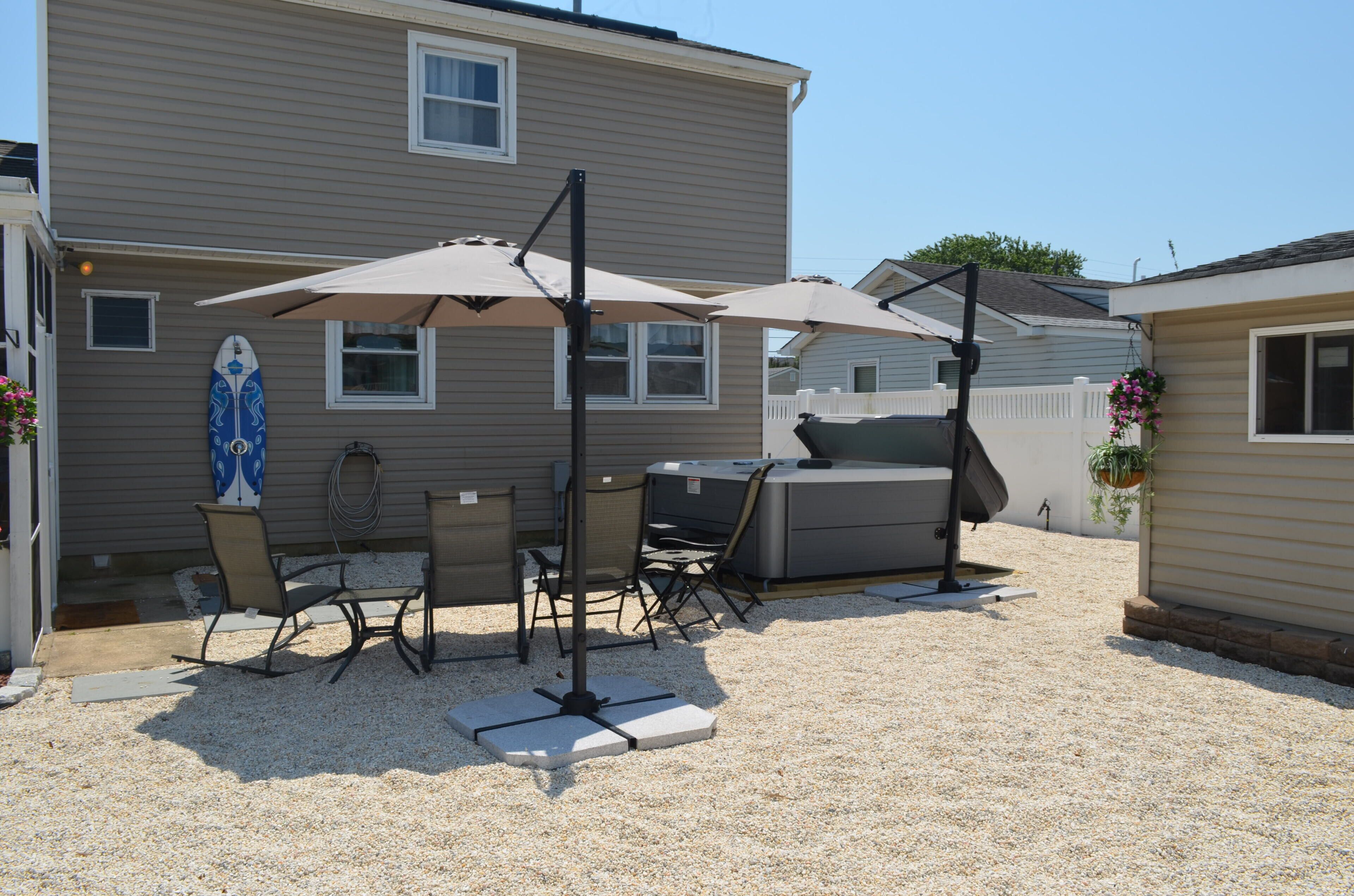 Un'area patio esterna con tavolo e sedie, un barbecue e un'asse di surf appoggiata alla casa.