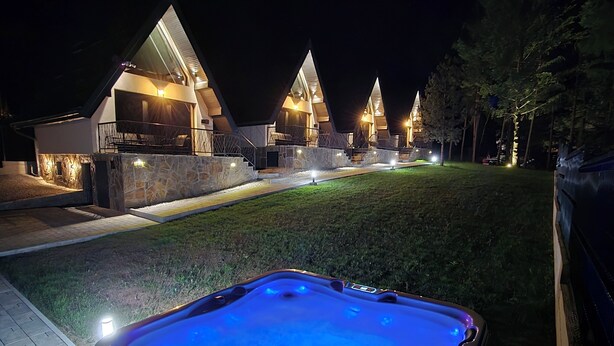 A hot tub with a blue light, a stone exterior, and a house with multiple triangular roofs.