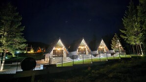 A row of triangular-roofed cabins with outdoor seating, surrounded by a fence and trees.