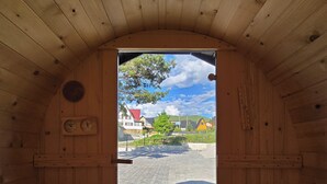 A wooden sauna room with benches, a stone floor, and a view of houses and trees outside.