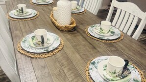 Une table à manger dressée avec des assiettes, des tasses et un vase contenant des fleurs séchées.