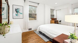 Ein Schlafzimmer mit einem Bett, einem Schreibtisch, einem Sessel, einer Lampe, einem Spiegel und Bildern an der Wand.