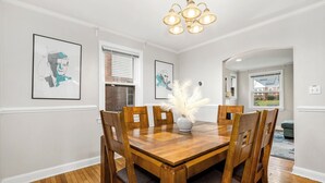 Ein Esszimmer mit Holztisch, Stühlen, einer Vase mit weißen Blumen und gerahmten Kunstwerken an den Wänden.