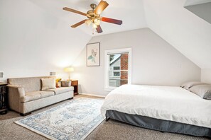 A bedroom with a bed, a ceiling fan, a window, a couch, a rug, and a lamp.