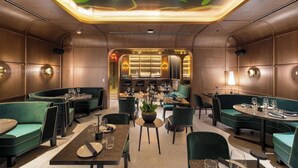 A restaurant with green upholstered booths and tables, a central bar area, and a ceiling with a green abstract design.