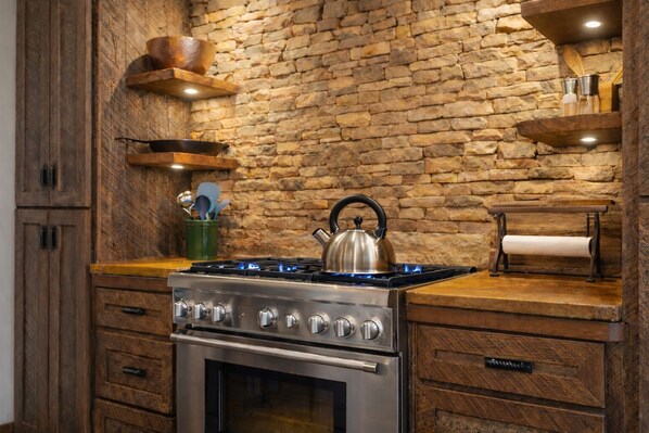 A kitchen with a stone wall, wooden cabinets, a gas stove, and a kettle.