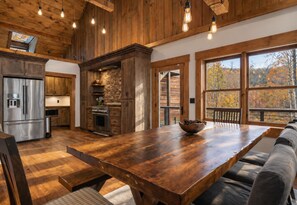 A spacious kitchen with wooden cabinets, a large wooden table, and a stone fireplace. - Creek Haüs: Cozy Retreat w/ Endless Entertainment • HotTub • FirePit • GameRoom (Blue Ridge)
