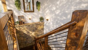 A wooden staircase with a stone wall and a small table with a plant on top. - Creek Haüs: Cozy Retreat w/ Endless Entertainment • HotTub • FirePit • GameRoom (Blue Ridge)
