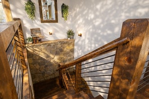 A wooden staircase with a stone wall and a small table with a plant on top.