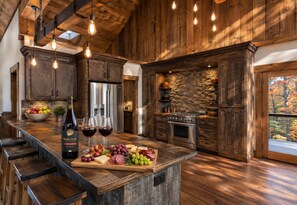 A kitchen with wooden cabinets, a stone wall, and a large island with a wine bottle and glasses. - Creek Haüs: Cozy Retreat w/ Endless Entertainment • HotTub • FirePit • GameRoom (Blue Ridge)
