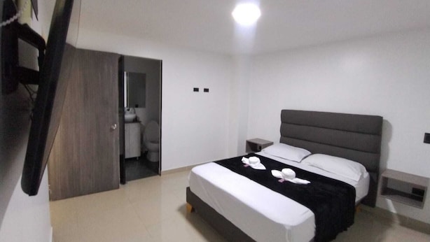 Ett modernt hotellrum med en stor säng, sängbord, en garderob och ett badrum som syns genom en öppen dörr.
