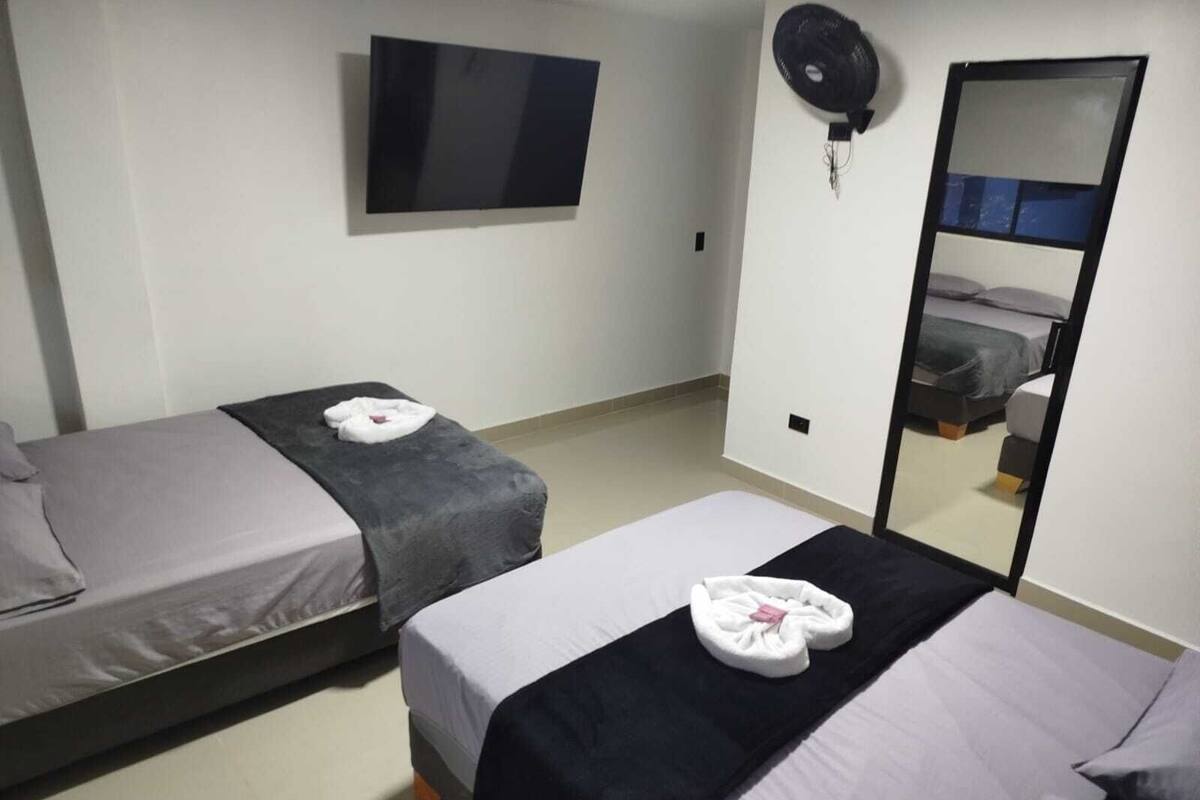 A hotel room with two beds, a flat-screen TV, a mirror, and a ceiling fan.