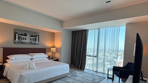 Une chambre d’hôtel moderne, dotée d’un grand lit, d’un bureau, d’une chaise et offrant une vue sur la ville par la fenêtre.