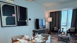 Une chambre d’hôtel moderne dotée d’un coin repas, d’un ensemble de canapés et d’une grande fenêtre avec des rideaux.