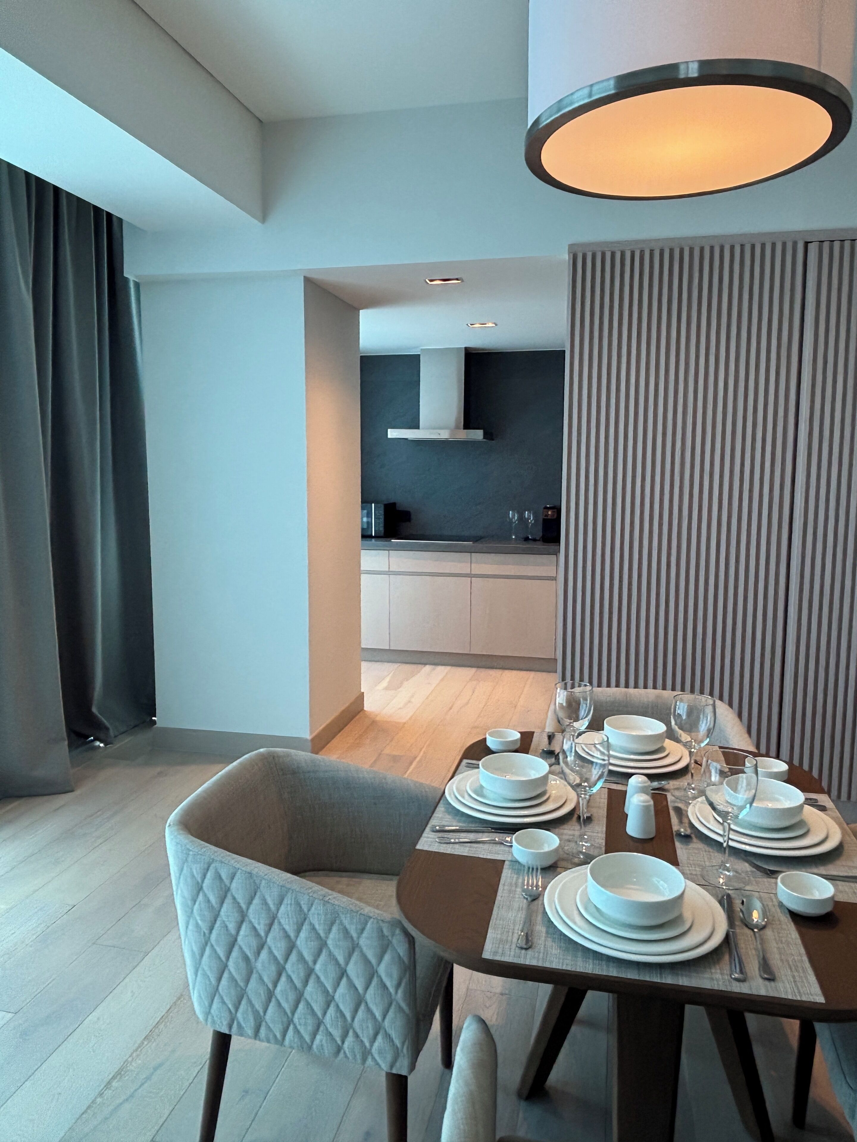 Un espace repas moderne avec une table en bois dressée pour quatre personnes, une chaise matelassée et une cuisine en arrière-plan.