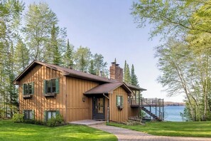 Een houten chalet met schoorsteen, terras en uitzicht op een meer.