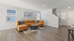Un salon spacieux avec un grand canapé d’angle, une table basse ronde et un plancher en bois franc.