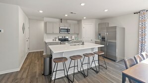 Une cuisine moderne dotée d’un îlot central, d’appareils électroménagers en acier inoxydable et de tabourets de bar en bois.
