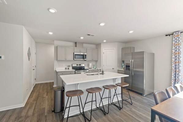 Una cocina moderna con una isla central, electrodomésticos de acero inoxidable y taburetes de madera.