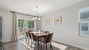Un espace repas comprenant une table et des chaises en bois, un lustre et une vue sur l’extérieur.