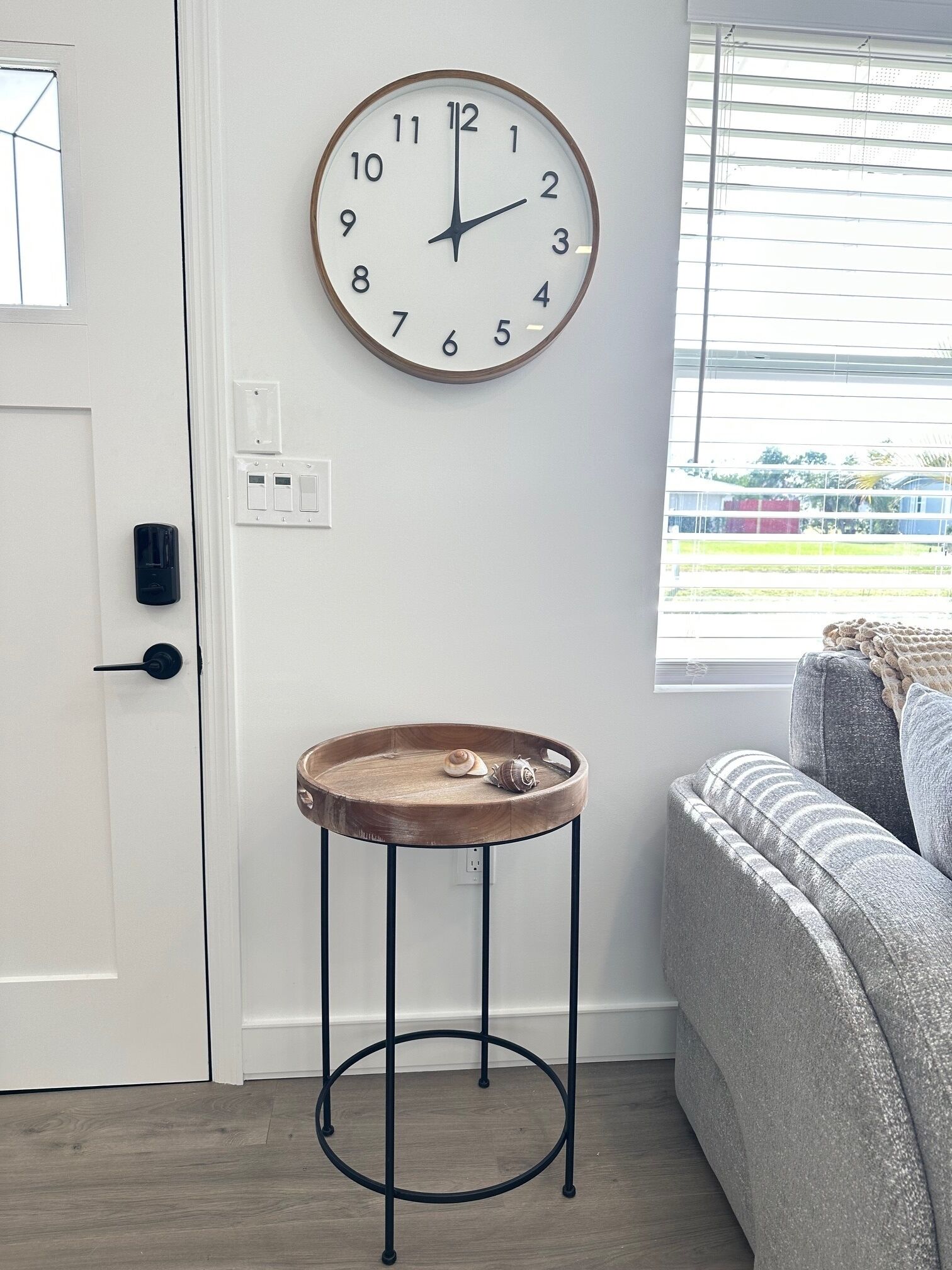 Een kamer met een ronde wandklok, een houten bijzettafeltje met een slak, en een grijze bank.