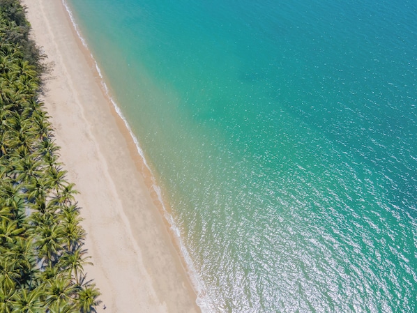 Vista aérea de uma praia com águas turquesa cristalinas e uma faixa de areia ladeada por palmeiras.