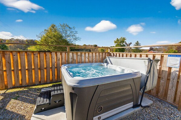 A hot tub in a backyard with a wooden fence and a sign about safety rules. - The Caboose + Pickleball, Hot Tub, Private Trail (Creola)