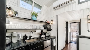 Une cuisine moderne avec des murs en bois peints en blanc, un plan de travail noir et un réfrigérateur en acier inoxydable. On y trouve des étagères avec de la verrerie et une plante en pot.