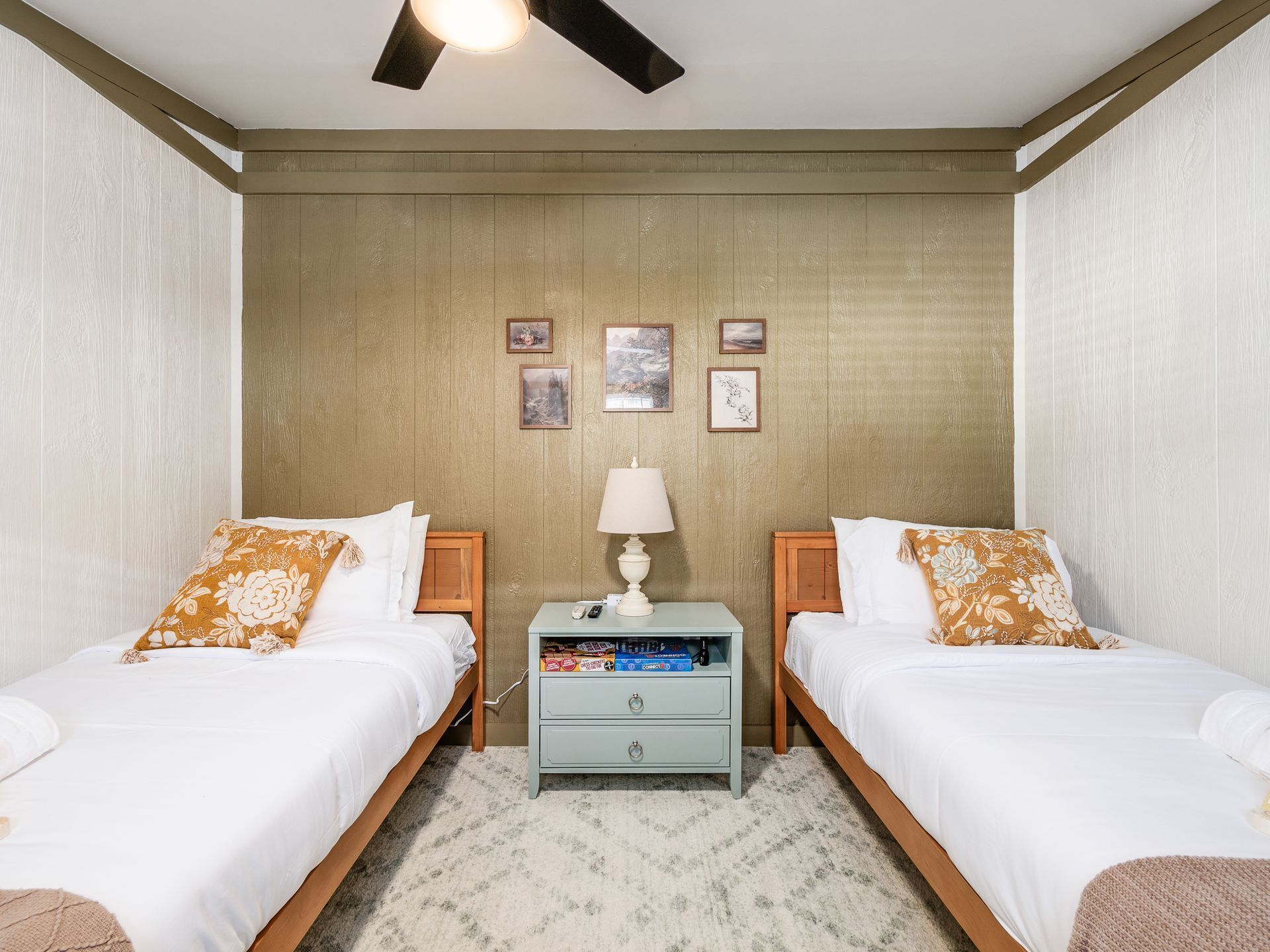 A hotel room with two beds, a nightstand with a lamp, and a small table with books.