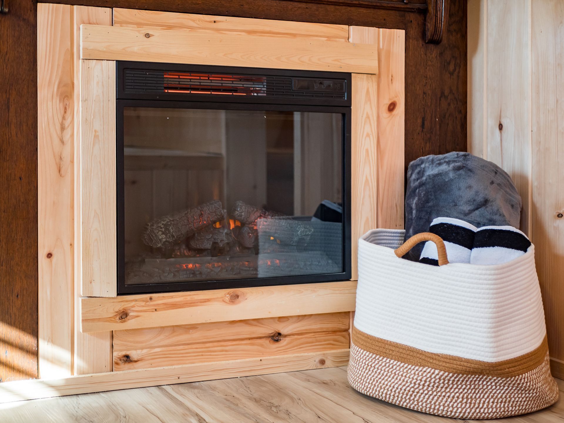 A wooden-framed fireplace with a glass door, a basket with a handle, and a grey blanket.