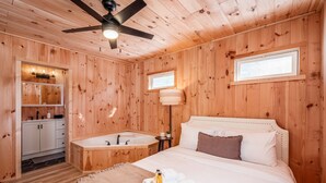 Ein Zimmer in einer Holzhütte mit einem Bett, einem Badezimmer mit Waschbecken und einem Deckenventilator.