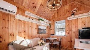 Ein gemütliches Blockhaus-Interieur mit einer Couch, einem Esstisch und einer Küchenzeile, mit Holzwänden und einem Deckenventilator.