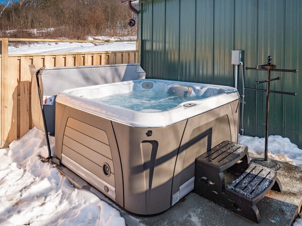 Ein Whirlpool in verschneiter Landschaft mit Holzterrasse und einem nahegelegenen Metallbau.