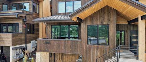 Une maison moderne à plusieurs étages, dotée d’une façade en bois, de grandes fenêtres et d’un escalier menant à l’entrée.