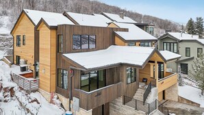 Una casa moderna de varios pisos con grandes ventanales, fachada de madera y techo cubierto de nieve.