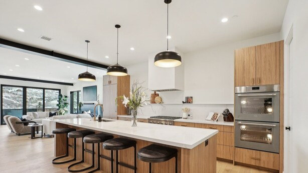 Una cocina moderna con una isla central, taburetes de bar, armarios de madera y electrodomésticos de acero inoxidable.