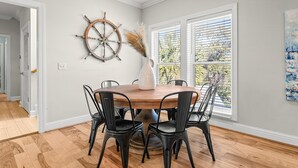 A dining area with a round wooden table, black chairs, a white vase with pampas grass, a ship's wheel, and a window with blinds. - C's The Day! Second to the beach, 3 Bed Plus loft (Panama City Beach)