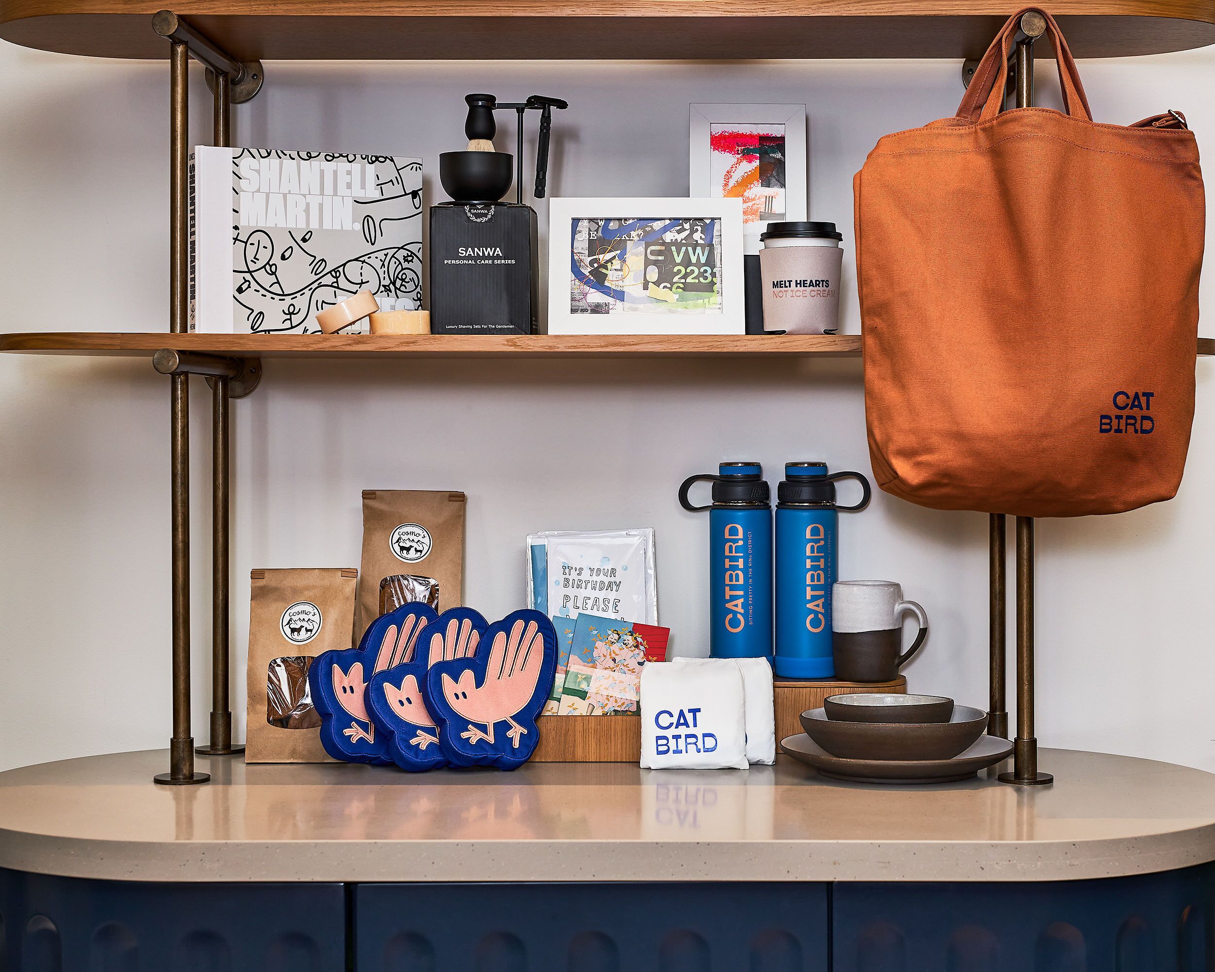 A shelf with a coffee maker, a personal care item, a birthday card, a tote bag, and a mug.