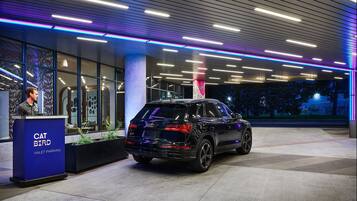 A black SUV parked at a modern building entrance with a blue and purple neon light design on the ceiling and a 'CAT BIRD VALET PARKING' sign.