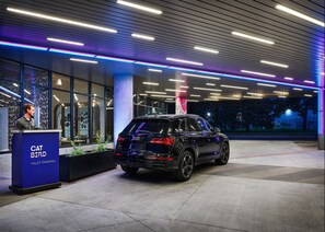 Un VUS noir était garé devant l’entrée d’un bâtiment moderne. Le plafond était décoré d’un éclairage néon bleu et violet, et un panneau indiquait : « CAT BIRD VALET PARKING ».