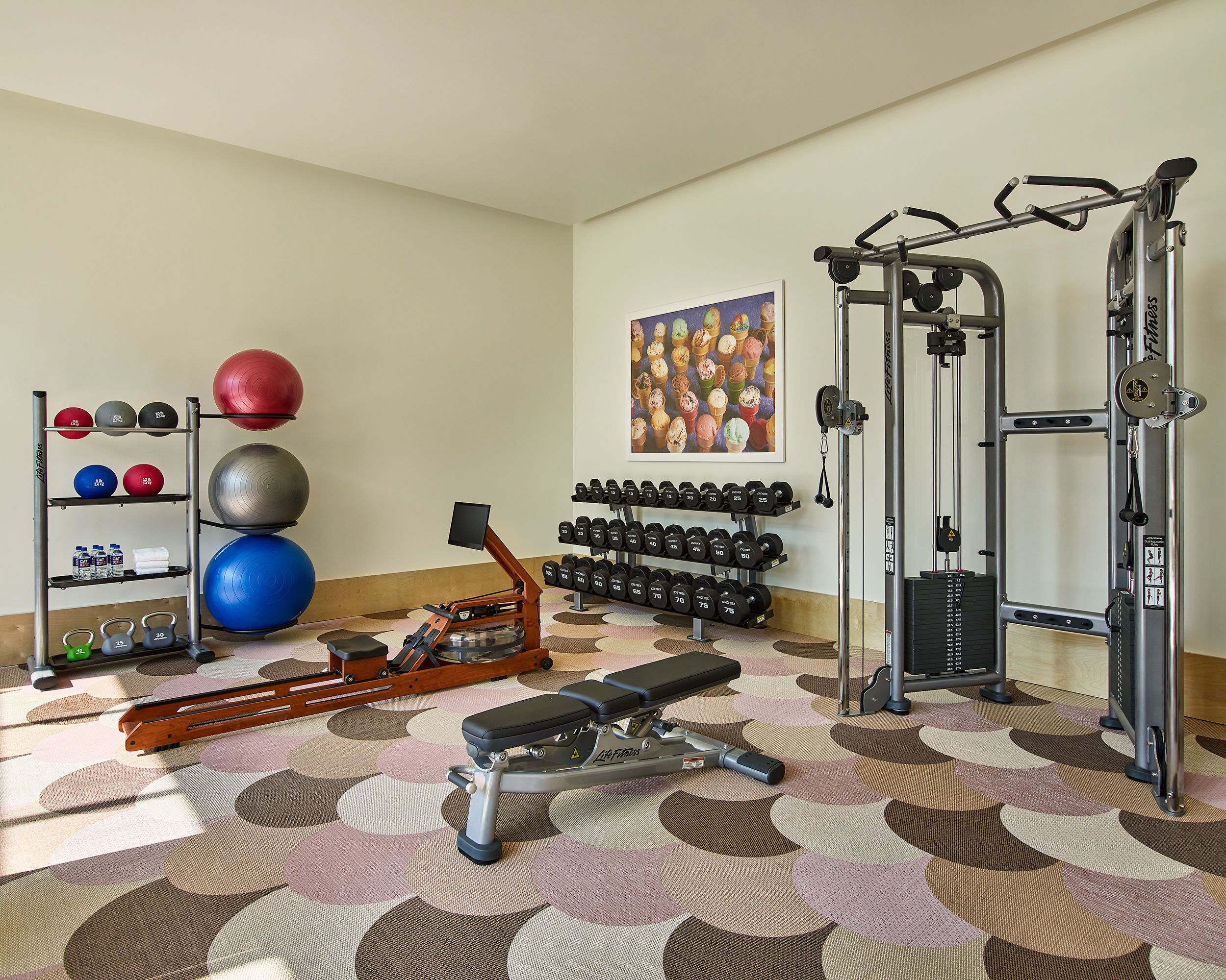 Un gimnasio con equipamiento de ejercicio, espacio para guardar pesas y piso estampado.